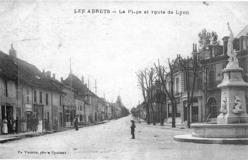 Carte postale ancienne Les Abrets, la place et route de Lyon en 1920, p 4 de L'Isère les 533 communes - photo F. Vialatte, Oyonnax.tiff
