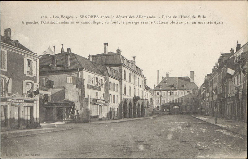 Carte postale ancienne Carte postale, Senones après le départ des Allemands, Place de l'Hôtel de Ville, A gauche, l'Ortskomandantur et camouflage, au fond, le passage ver