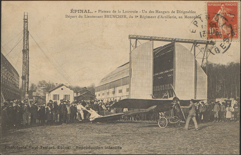 Carte postale ancienne Carte postale, Epinal, Plateau de la Louvroie, Un des Hangars de Dirigeables, Départ du Lieutenant Bruncher, du 8e Régiment d'Artillerie en monoplan